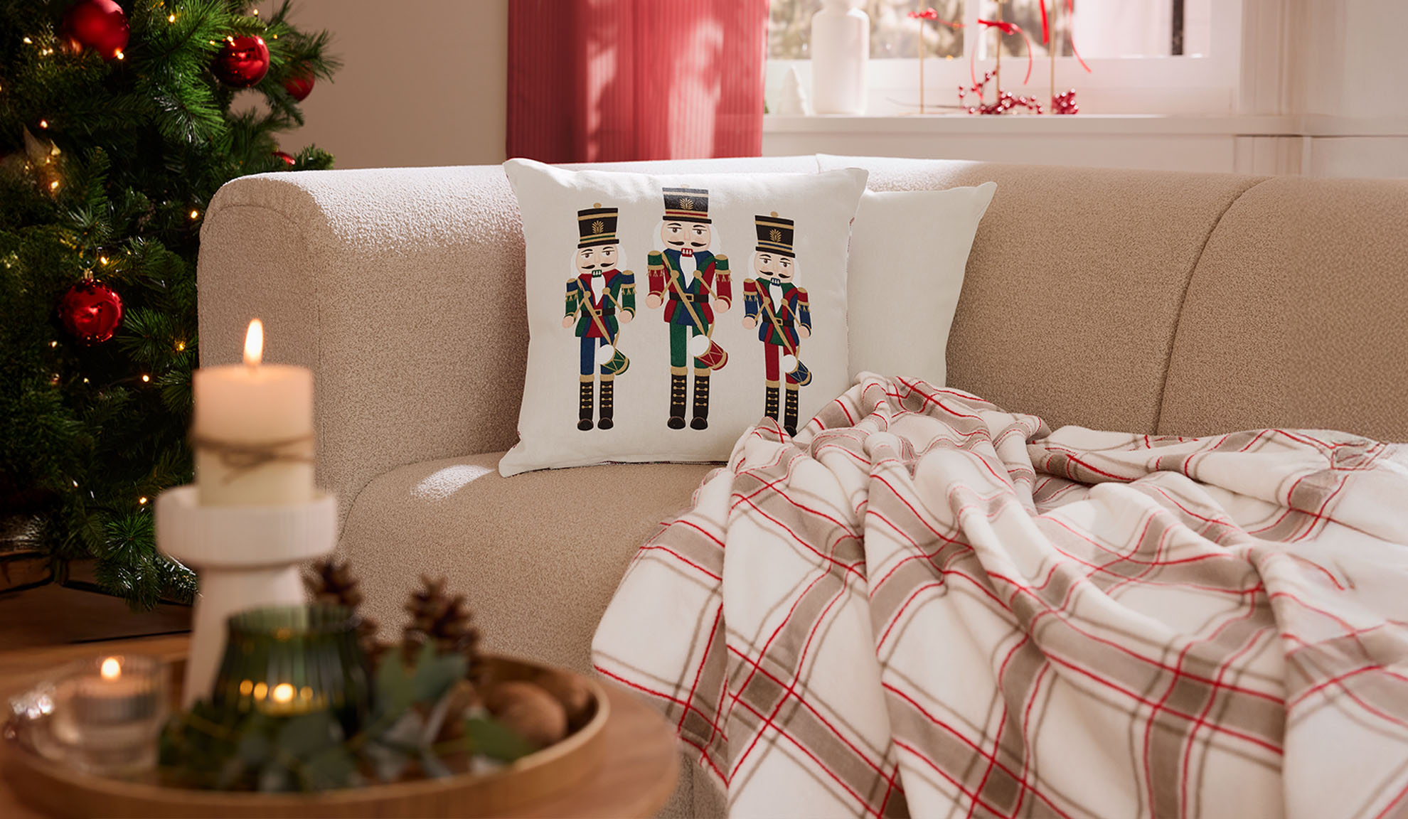 Soggiorno natalizio con divano, cuscini schiaccianoci, plaid a quadri e candele.