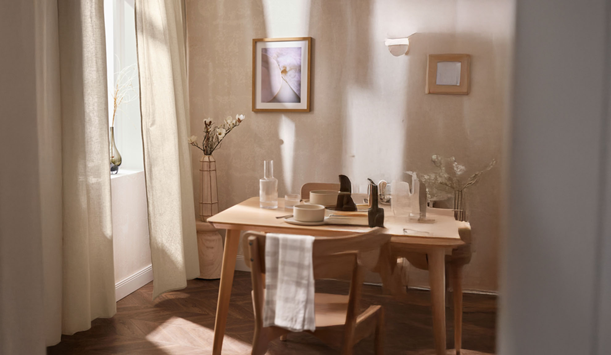 Una sala da pranzo con un tavolo di legno apparecchiato per due, con decorazioni chiare e luce naturale.