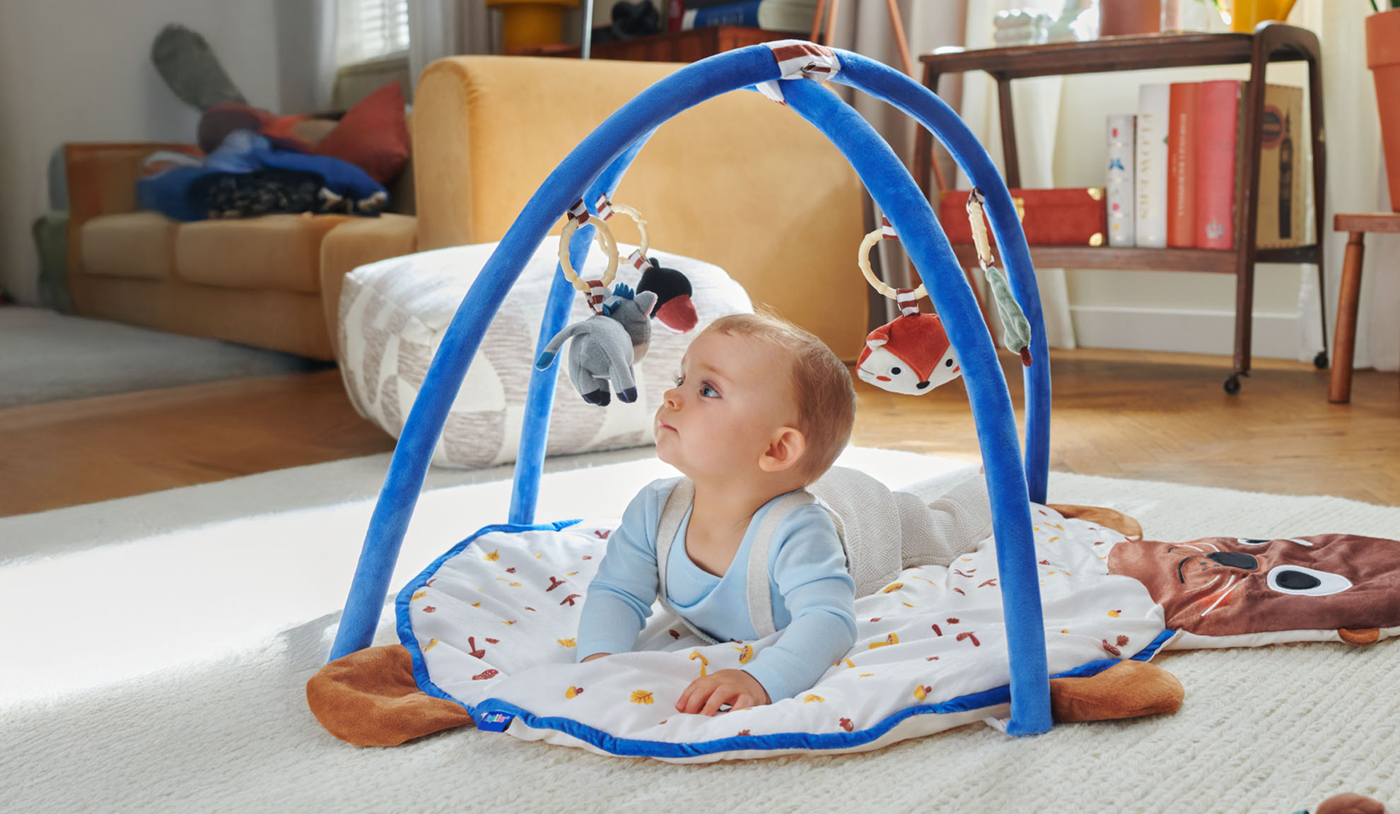 Un bambino gioca su un tappetino da gioco Tiny Love con arco a forma di animali.