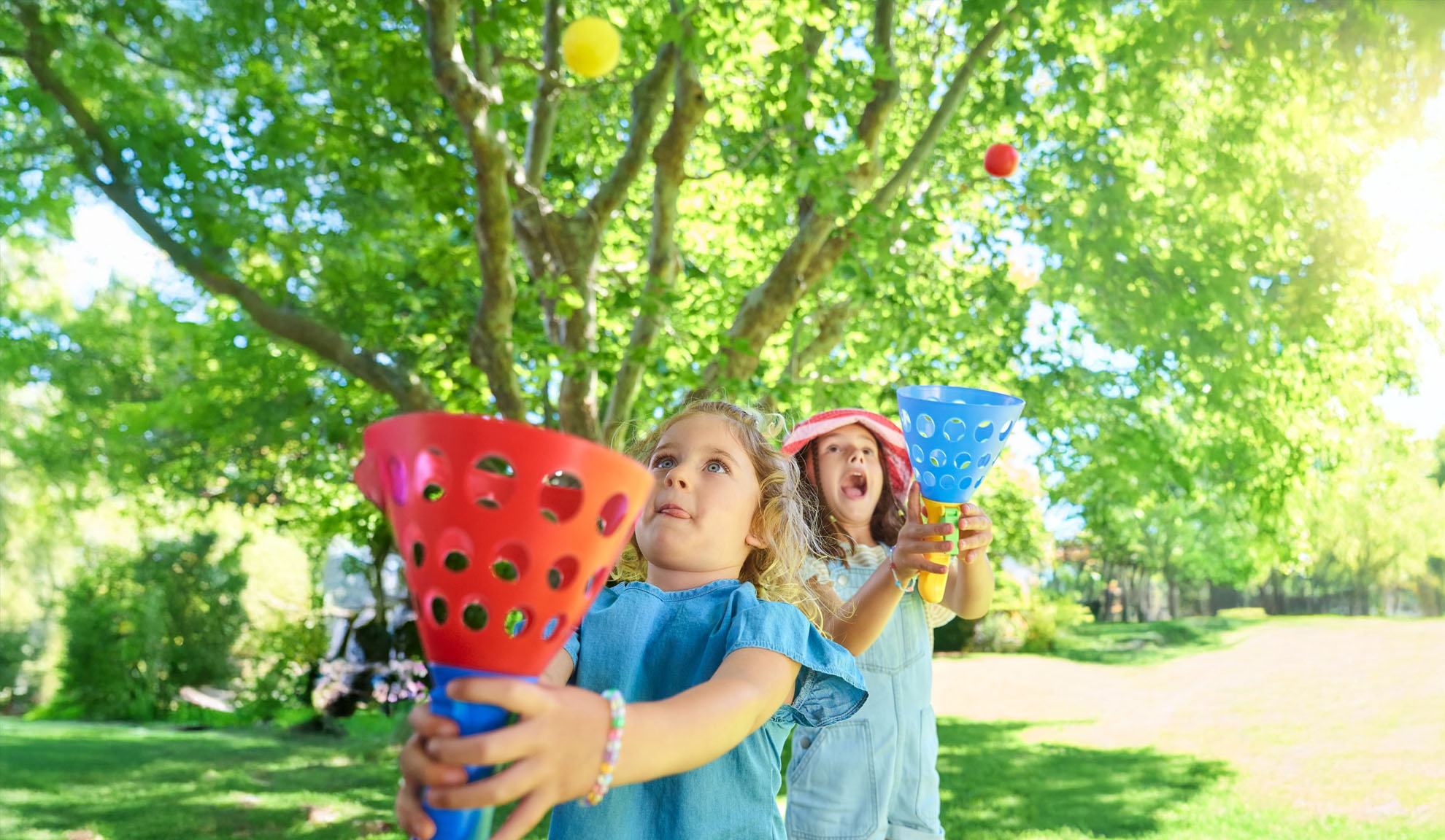 Due ragazze giocano a un gioco di presa all'aperto con raccoglitori di plastica colorati e palline.