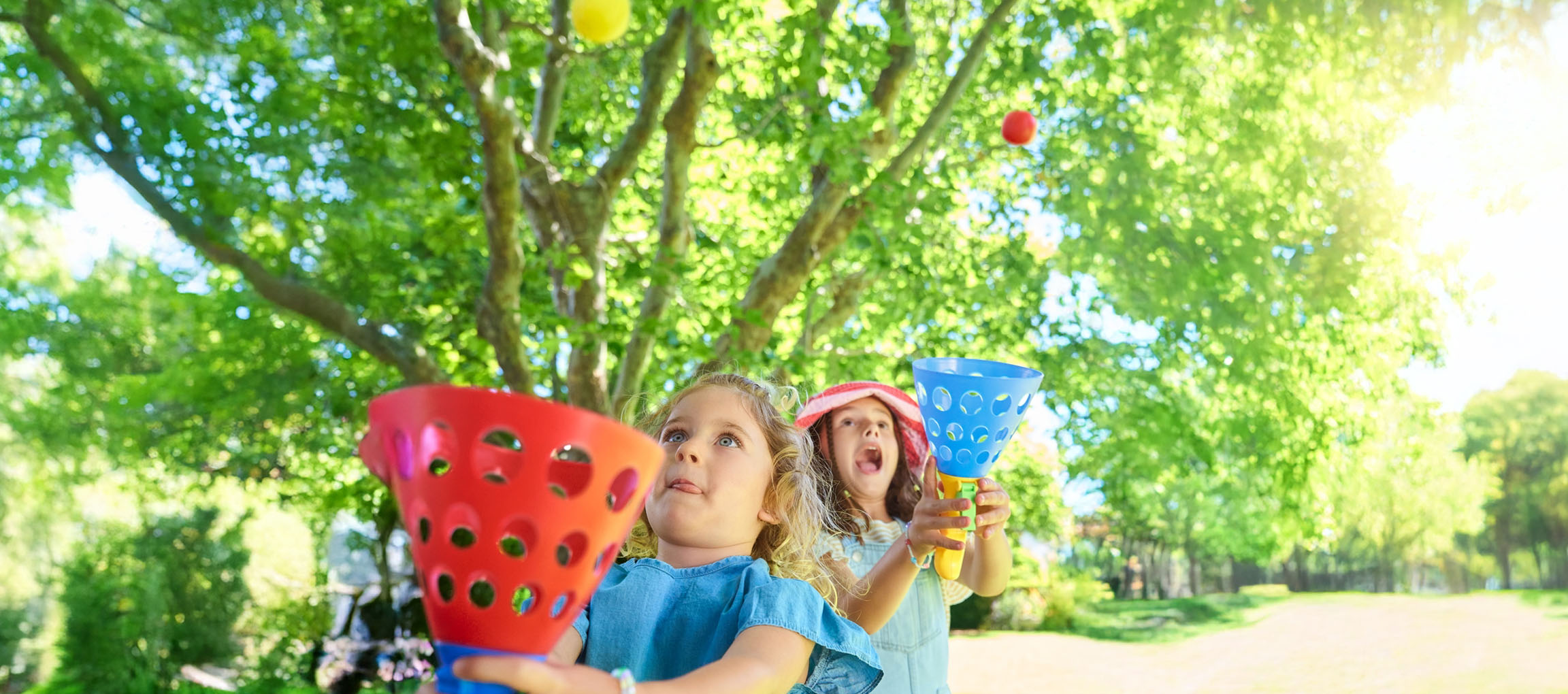 Due bambine giocano a lanciare palline in un parco assolato.
