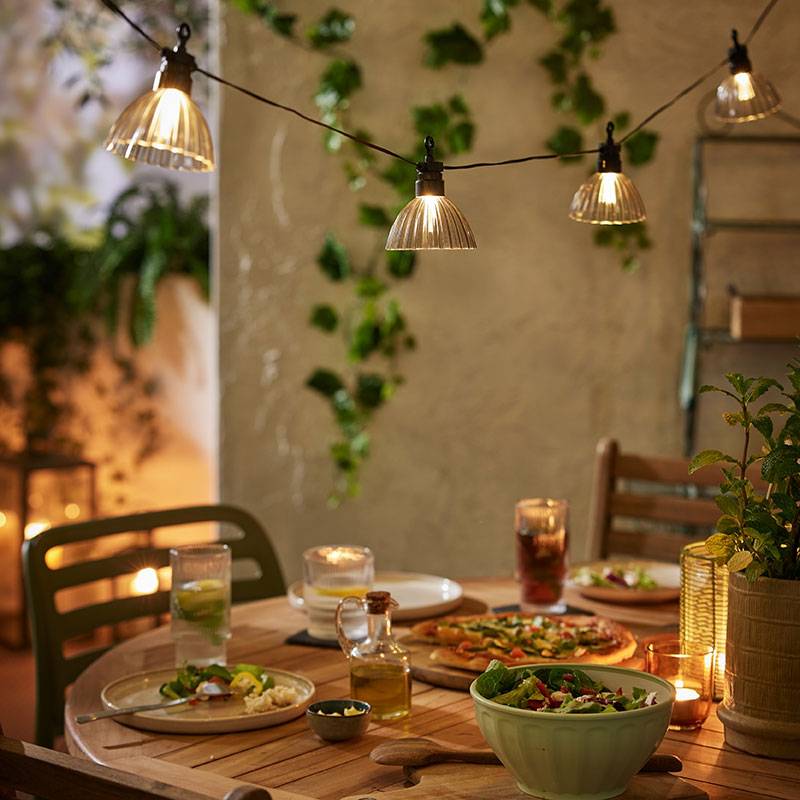 Illuminazione esterna con luci calde sopra un tavolo di legno con del cibo.
