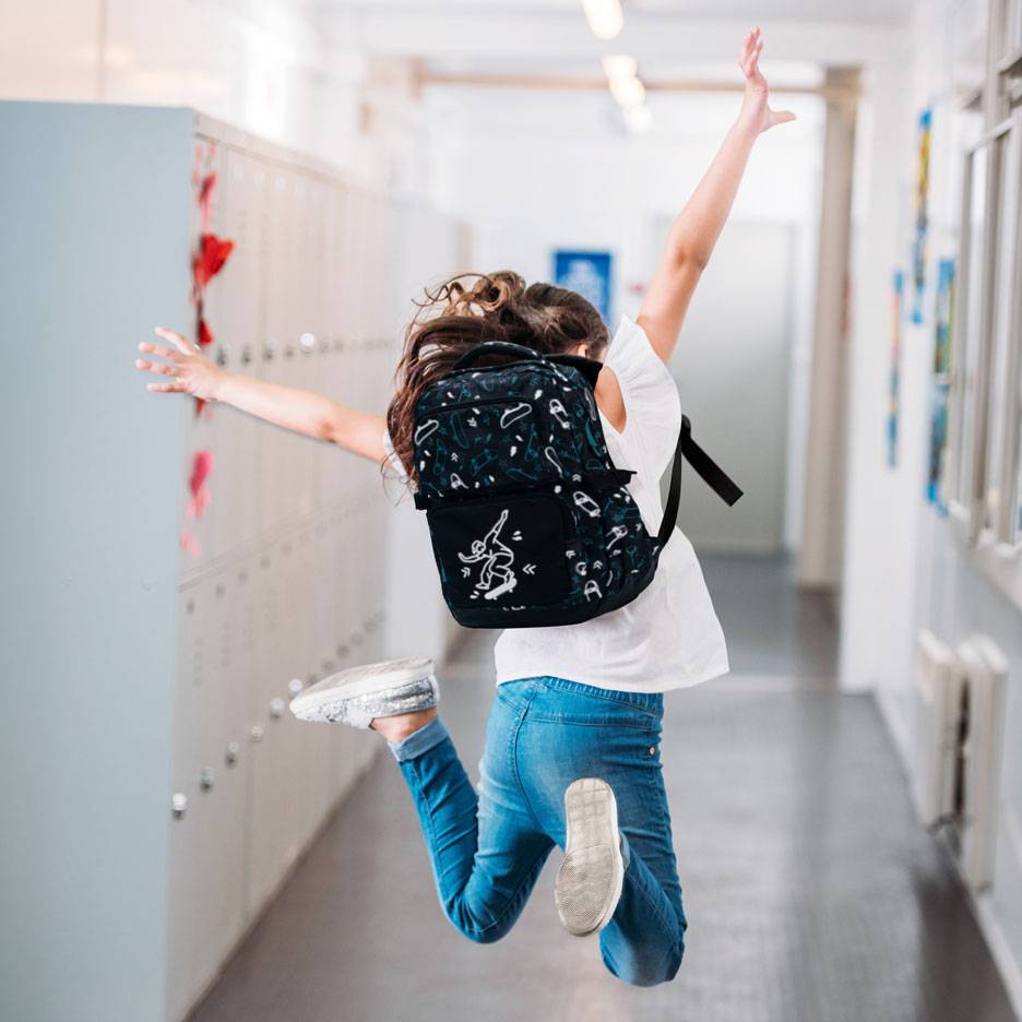 Bambino con zaino che salta in un corridoio scolastico.