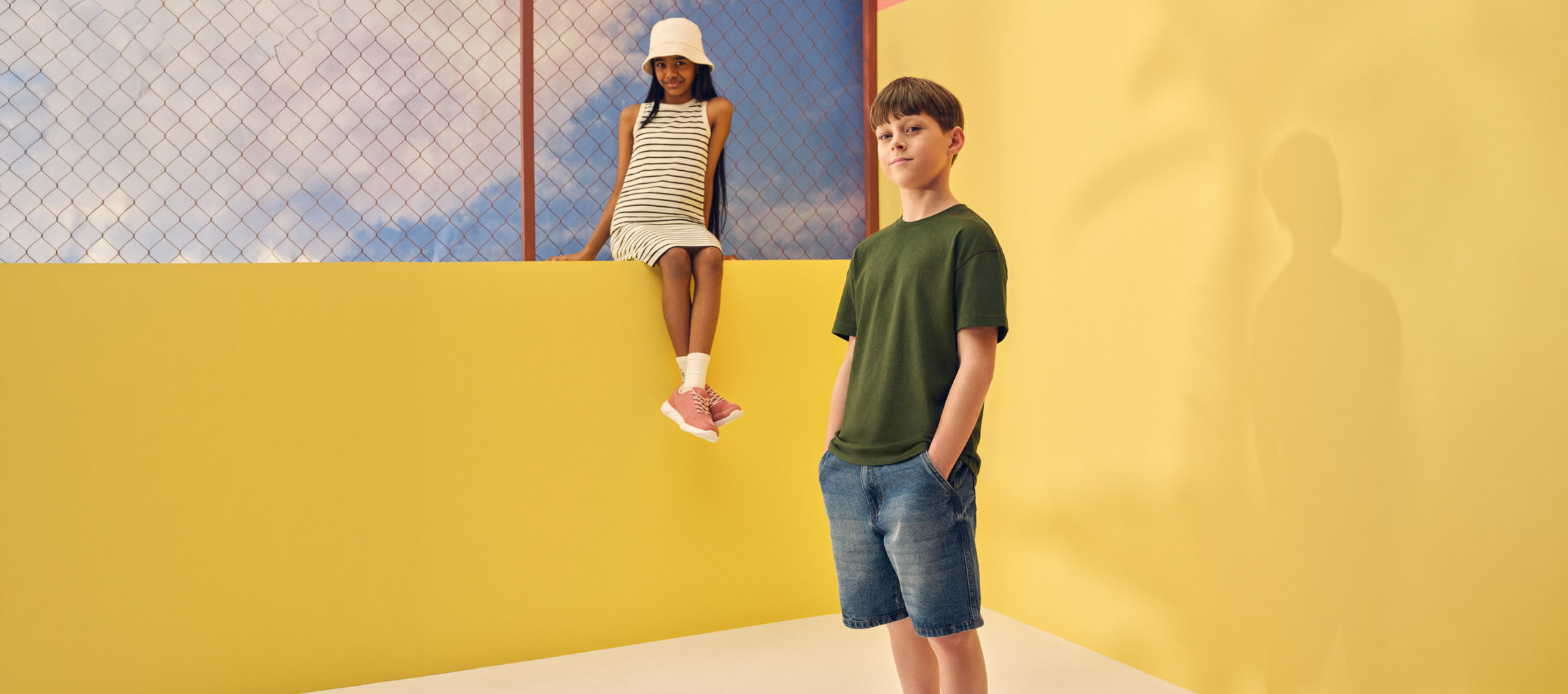 Due bambini in abiti estivi casual: una ragazza in abito a righe e un ragazzo in maglietta verde e pantaloncini di jeans.