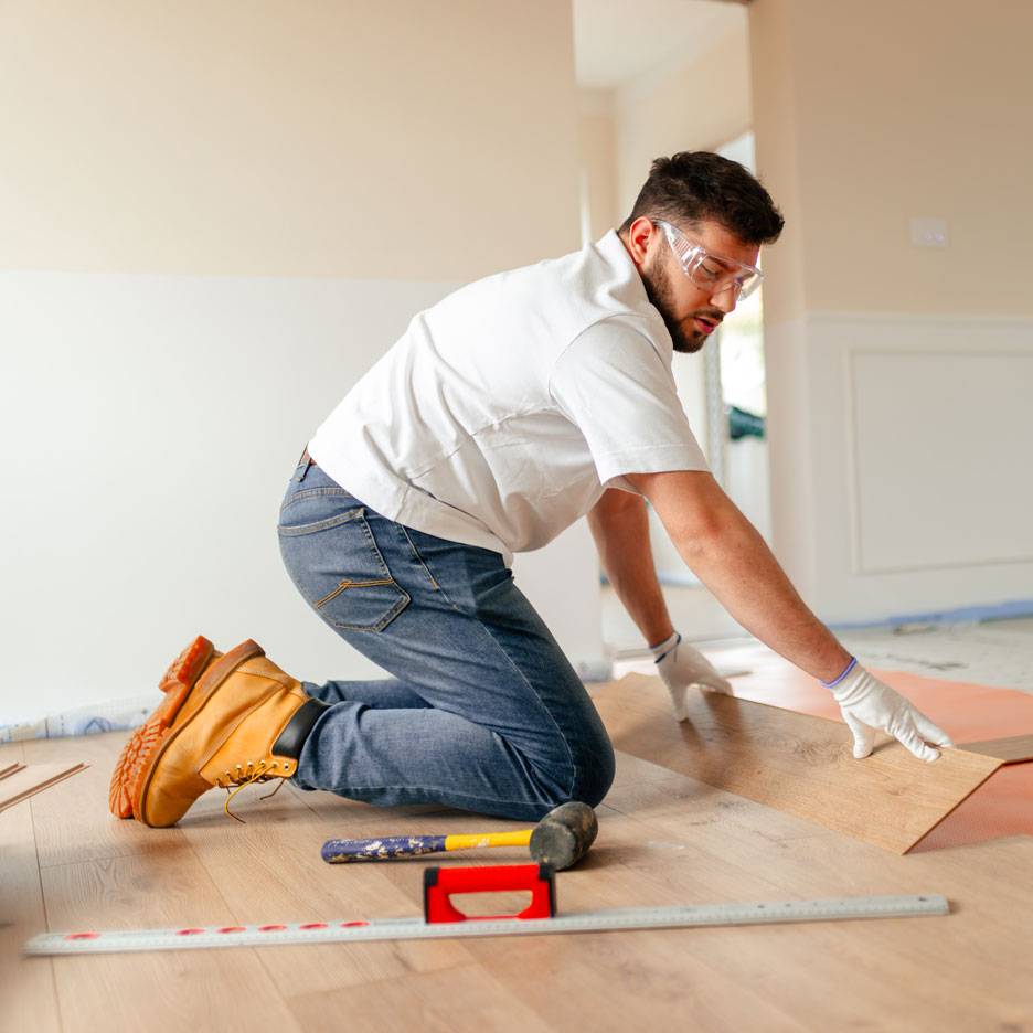 Uomo che posa il pavimento laminato, con occhiali di sicurezza e scarponi da lavoro.