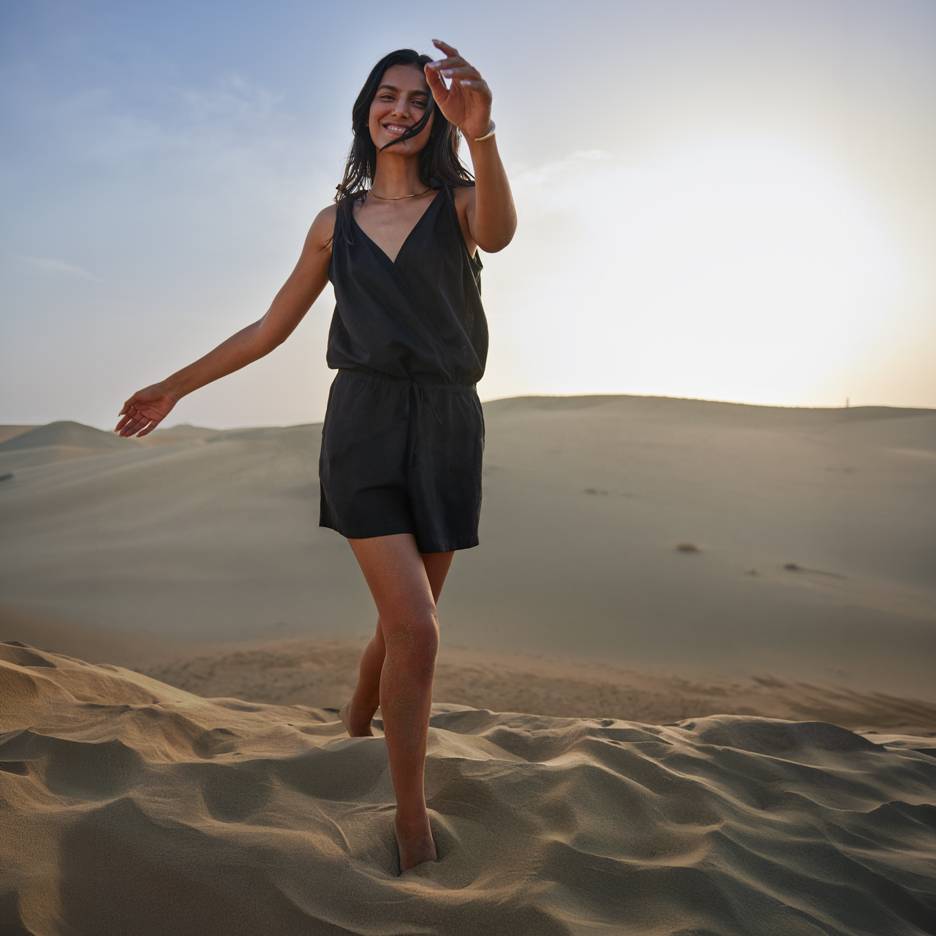 Donna in tuta nera a piedi nudi in piedi sulle dune di sabbia al tramonto.