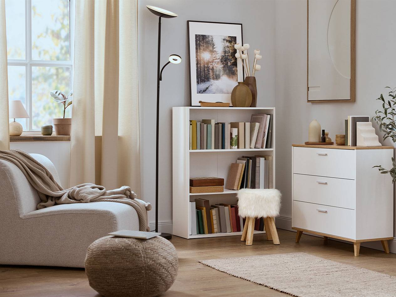 Soggiorno accogliente con poltrona, libreria e cassettiera in colori neutri.