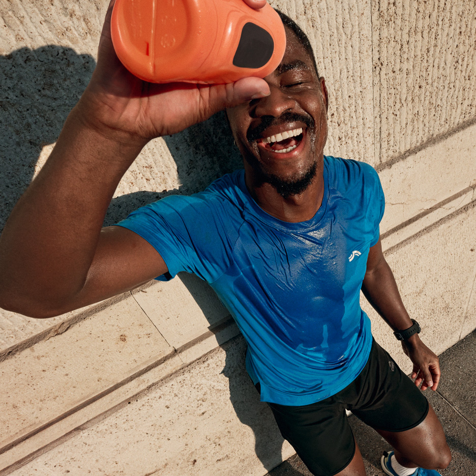 Uomo in maglietta sportiva blu e pantaloncini neri che si versa acqua dopo l'allenamento.