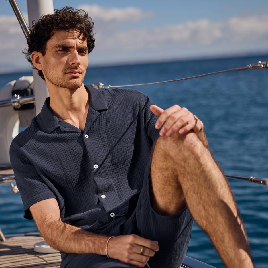 Uomo in camicia e pantaloncini blu scuro su uno yacht, che guarda il mare.