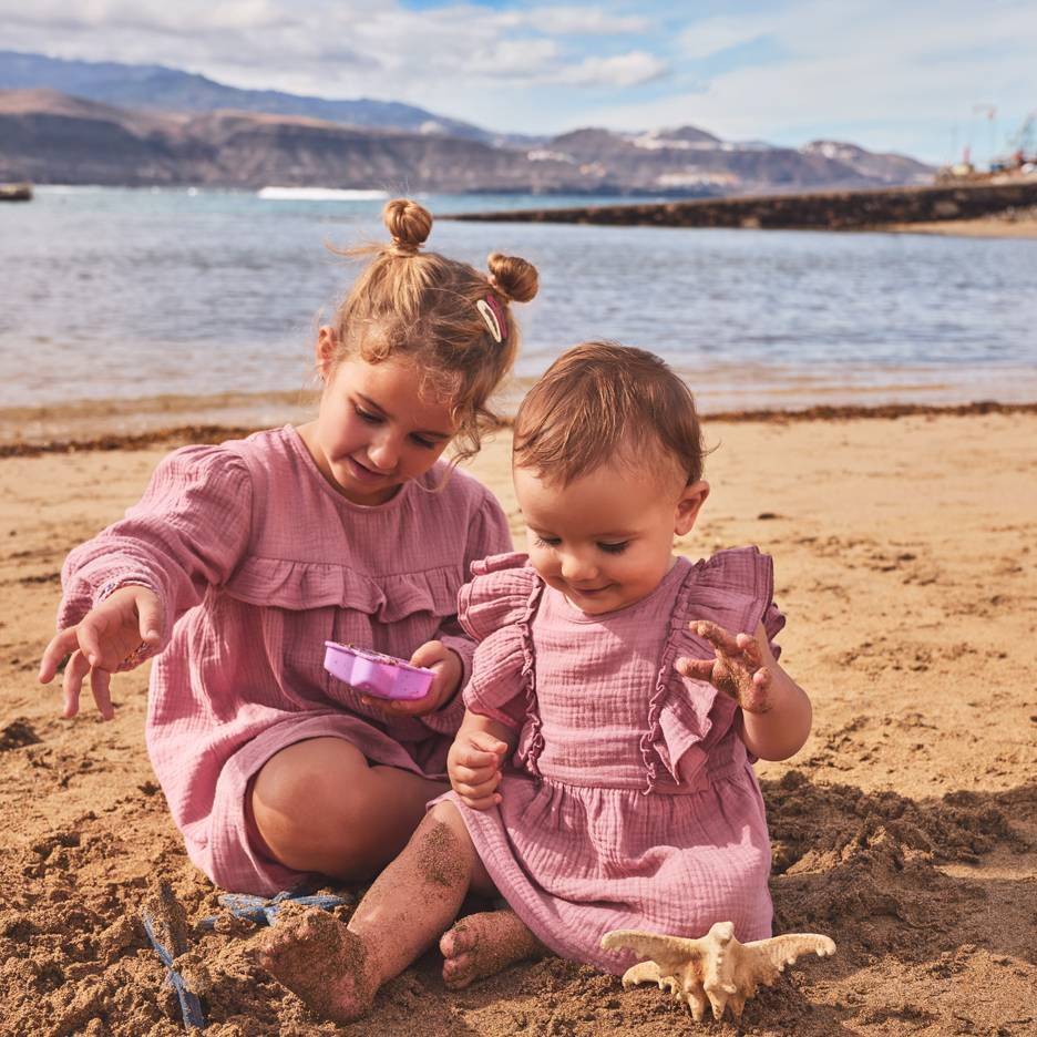 Due bambine in abiti rosa giocano nella sabbia in spiaggia.