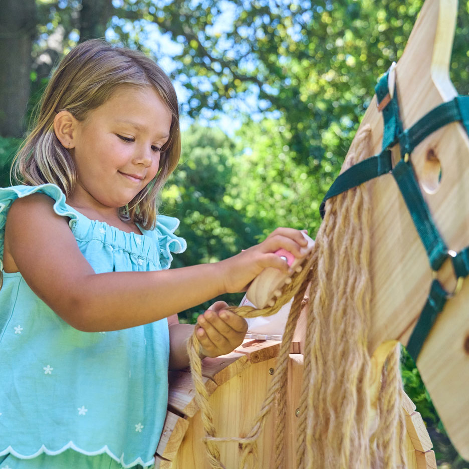 Bambina che spazzola la criniera di un cavallo a dondolo di legno all'aperto.