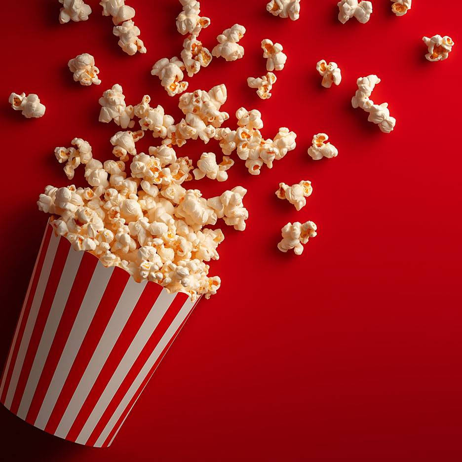 Popcorn su sfondo rosso, parte del popcorn in un contenitore di cartone a strisce.