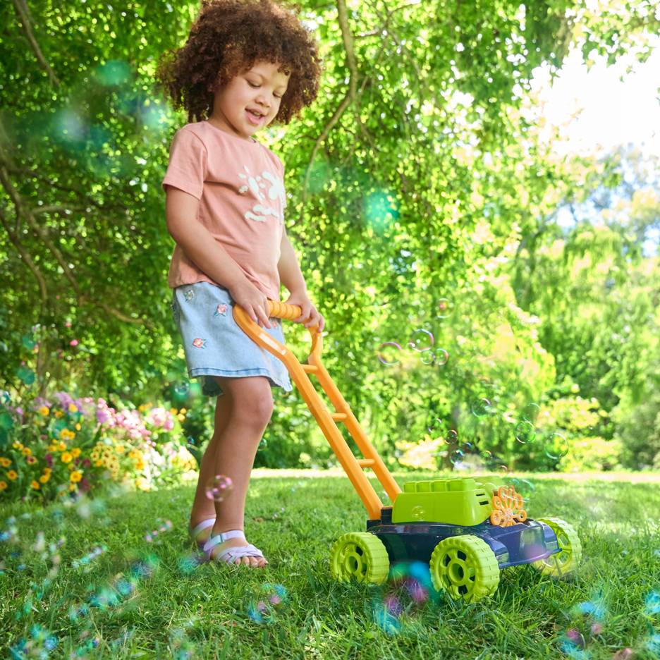 Un bambino con i capelli ricci spinge un tosaerba giocattolo che fa bolle sull'erba verde.