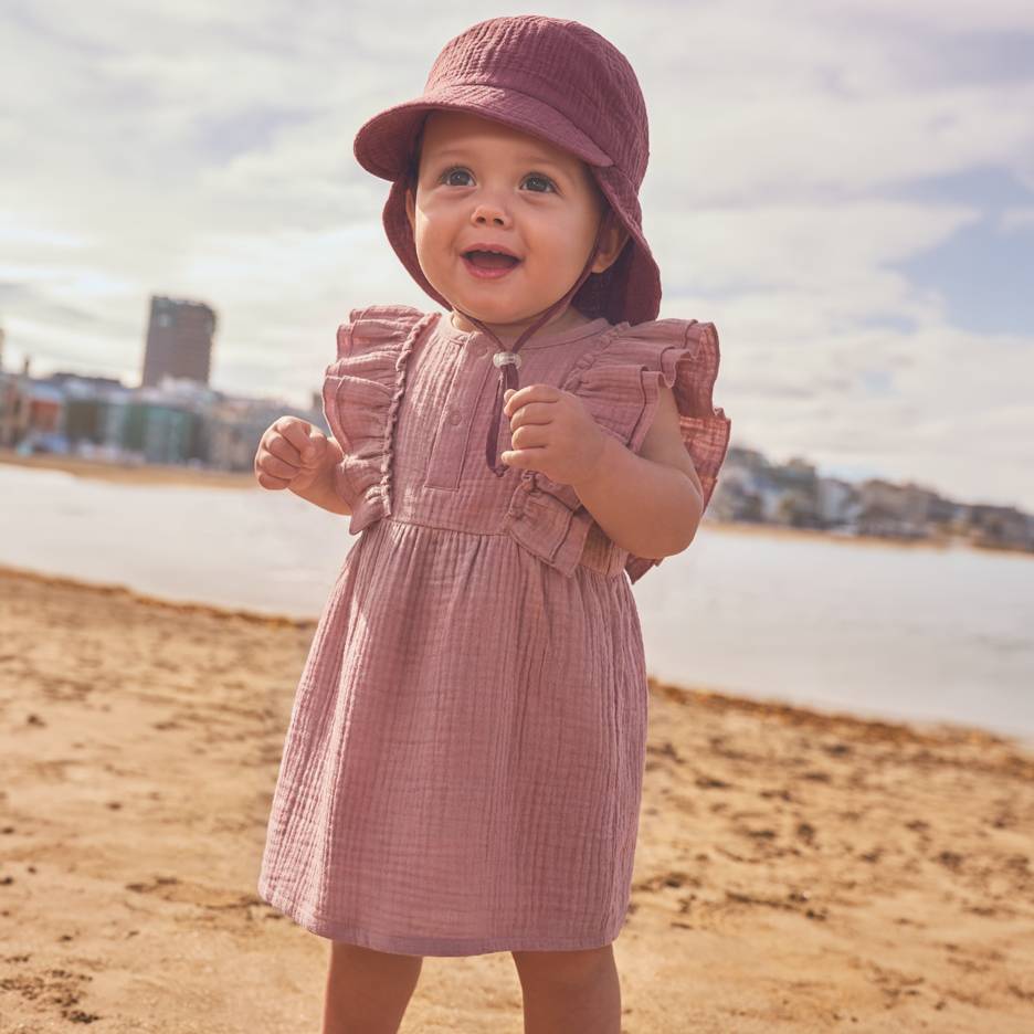 Bambina in vestito rosa e cappello in spiaggia.