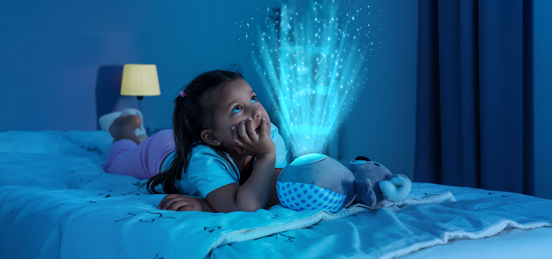 Bambina sdraiata a letto, guarda un proiettore di stelle che illumina la parete.