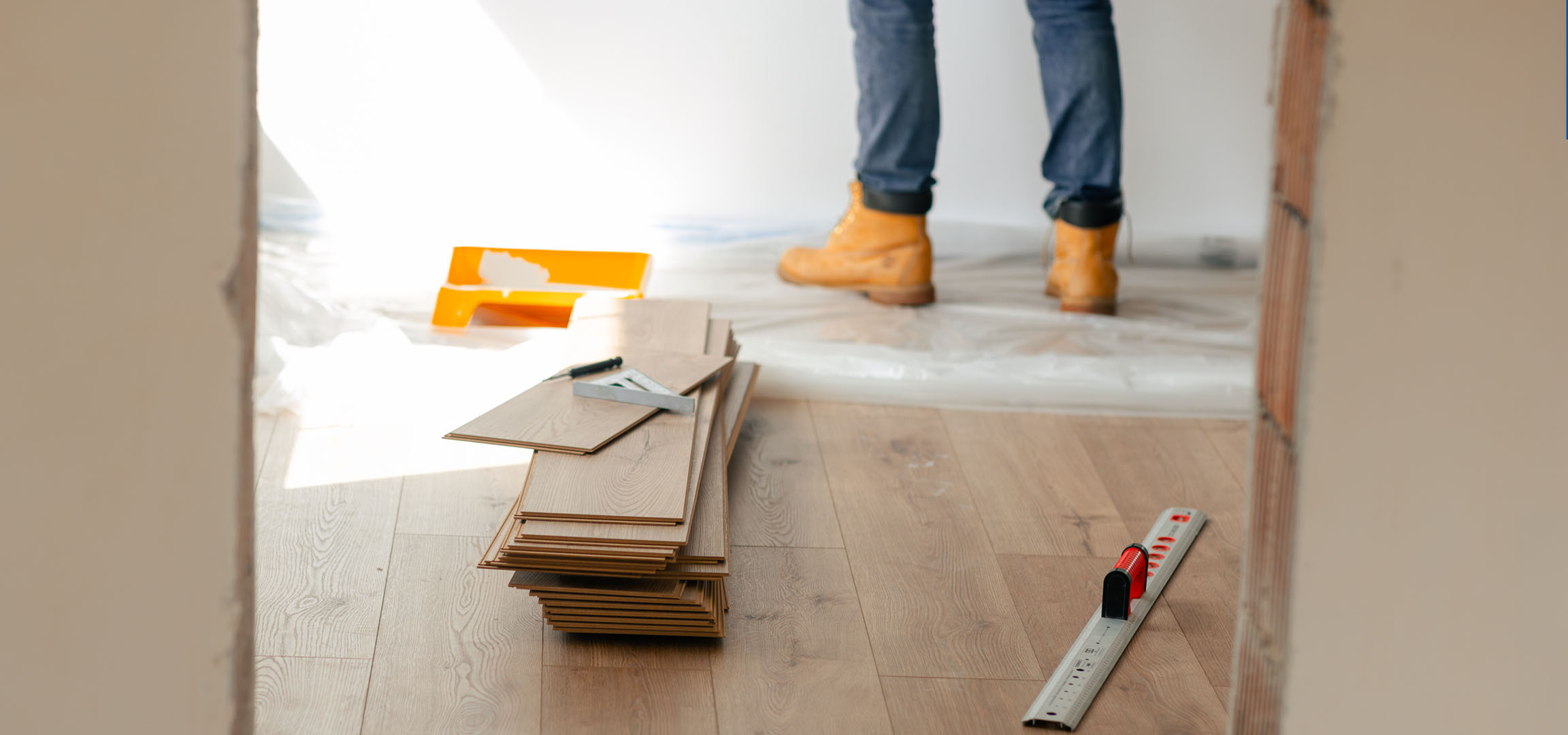 Tavole di pavimento laminato e attrezzi per l'installazione su un pavimento in legno, con una persona in stivali.