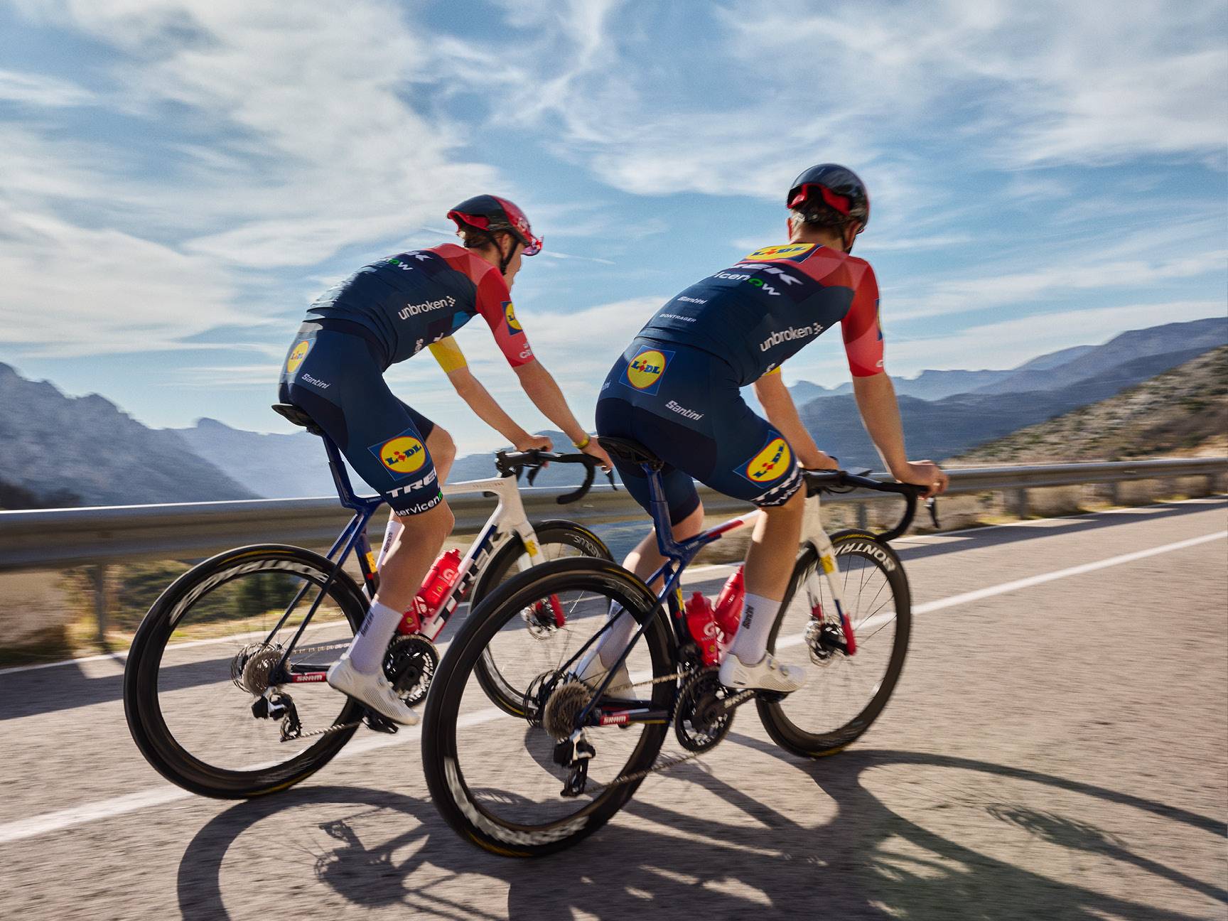 Due ciclisti in maglie e pantaloncini da ciclismo blu e rossi su una strada di montagna.