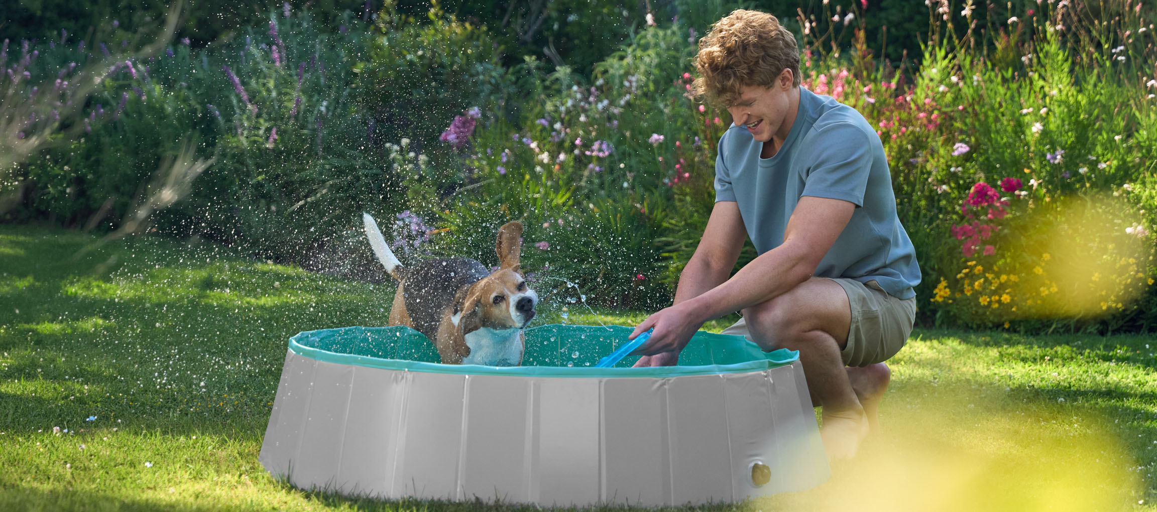 Uomo e cane giocano in una piscina per bambini in giardino.